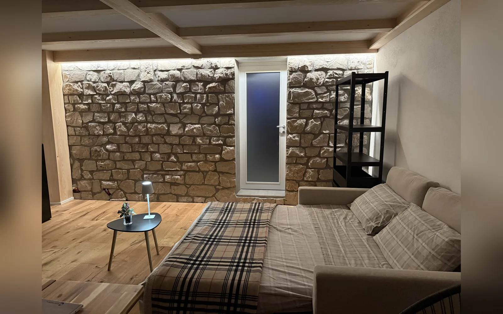 Der Wohnbereich des Studios mit Schlafsofa, sichtbarer Steinwand und Holzbalken