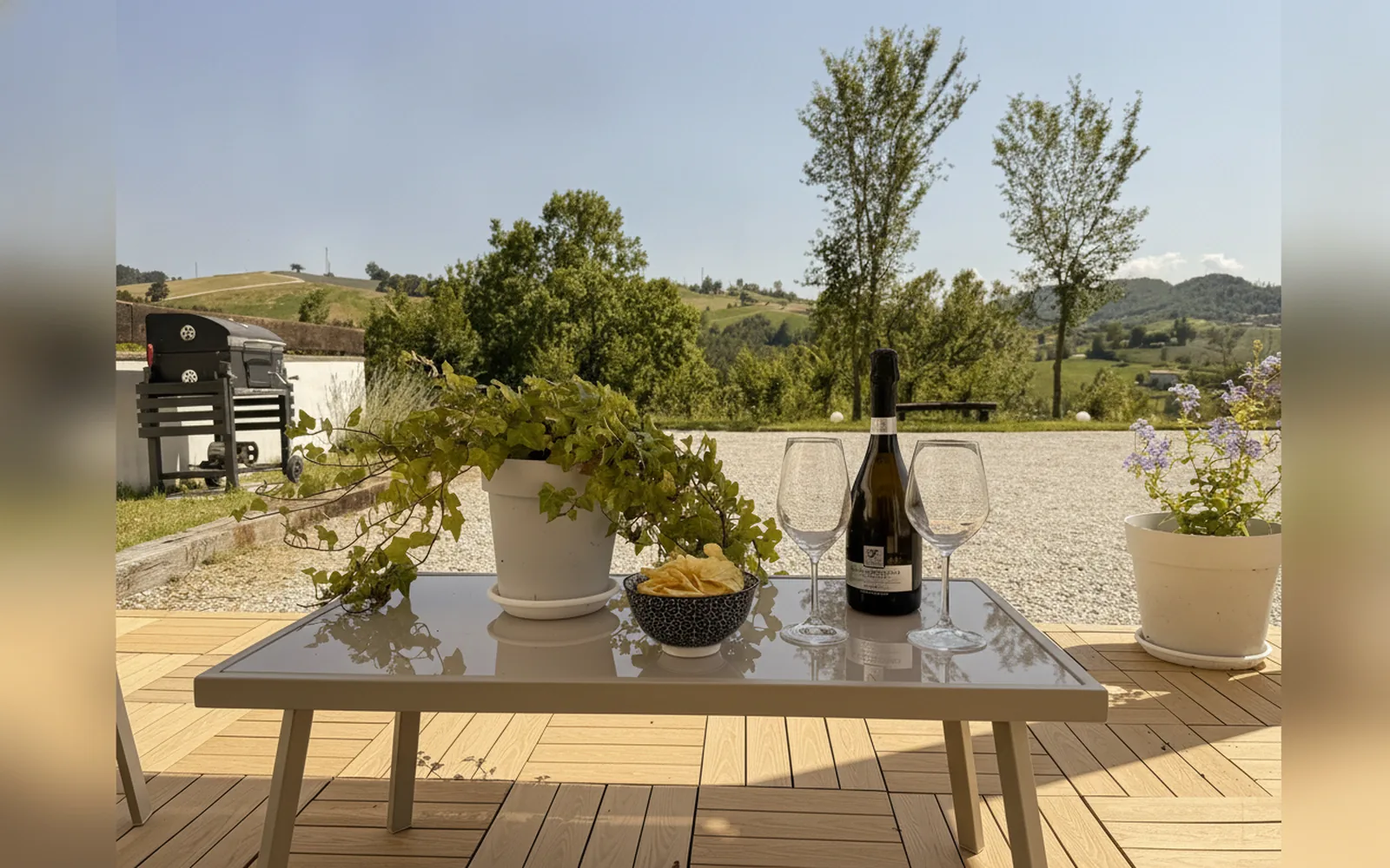 Der gedeckte Terrassentisch mit Gläsern und Flasche, vor den Hügeln